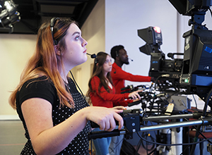 Communication student running camera in the news room on campus.