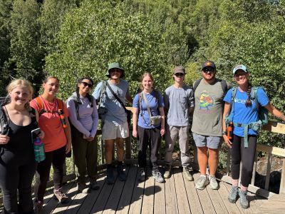 Eight students standing on a deck with vegetation in the background