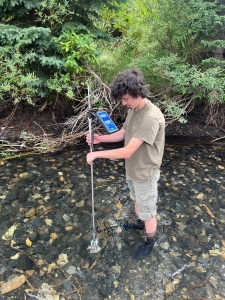 Male student taking water quality measurements in a stream