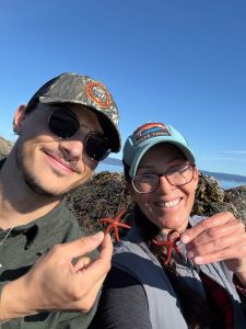 Two students smiling at the camera while each holds a starfish