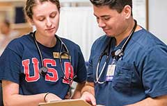 Student wth USA shirt talking to man with scrubs on looking at chart.