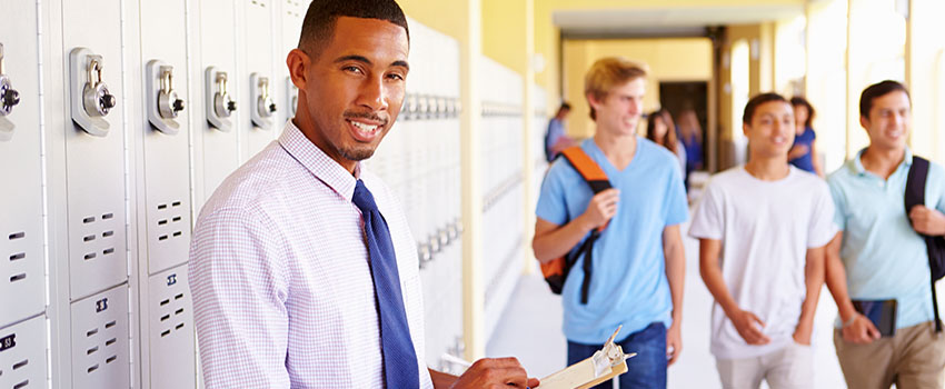 Man holding clipboard in front of lockers in school hallway.