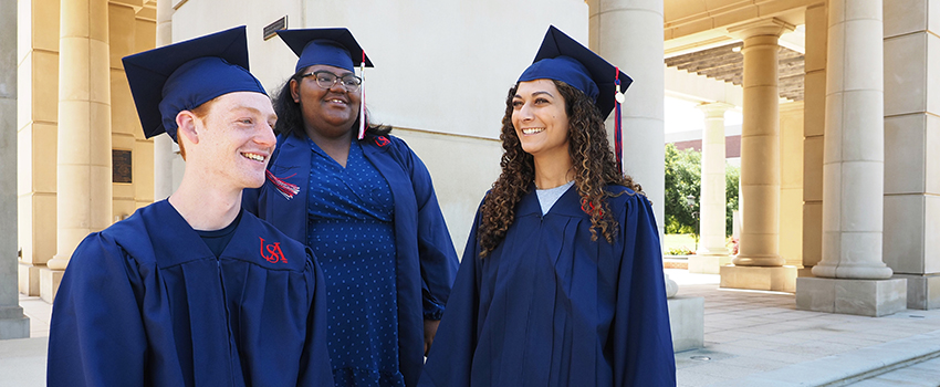 Three USA graduates in their cap and gowns smiling.