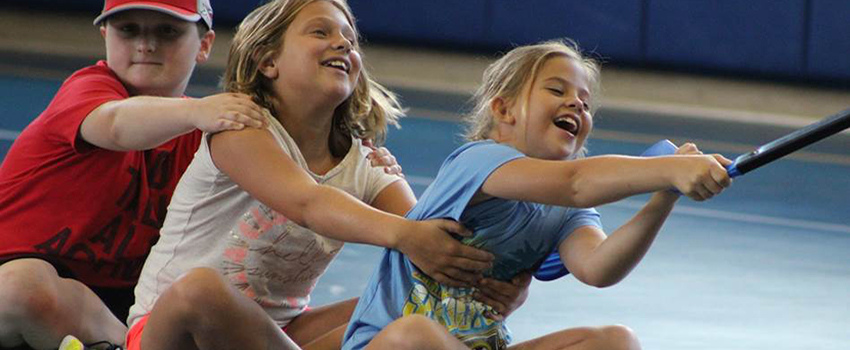 Kids sitting on rolling seat pulling rope in gym.