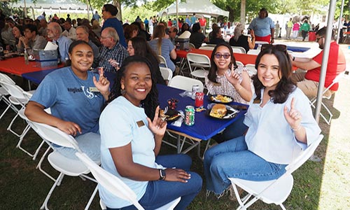 Employees holding up J sign at table during picnic.