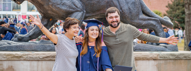 Student at graduation with parents in front of Jaguar statue.